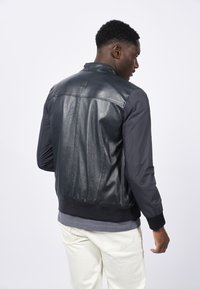 Chaqueta bomber de cuero negro y tejido con un dobladillo acanalado, textura suave y un detalle de etiqueta en la parte posterior. Diseñada para un ajuste moderno.