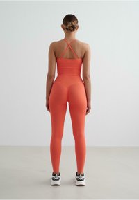 Set di abbigliamento sportivo arancione composto da un reggiseno sportivo aderente con spalline incrociate e leggings a vita alta. Il materiale sembra morbido ed elastico.