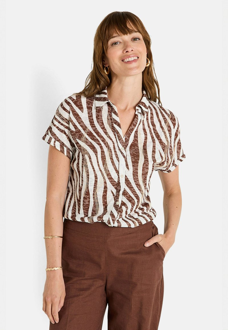 Camisa de manga corta con un patrón de rayas de cebra marrón y blanco, con un cierre de botones en el frente y un corte relajado, combinada con pantalones marrones.