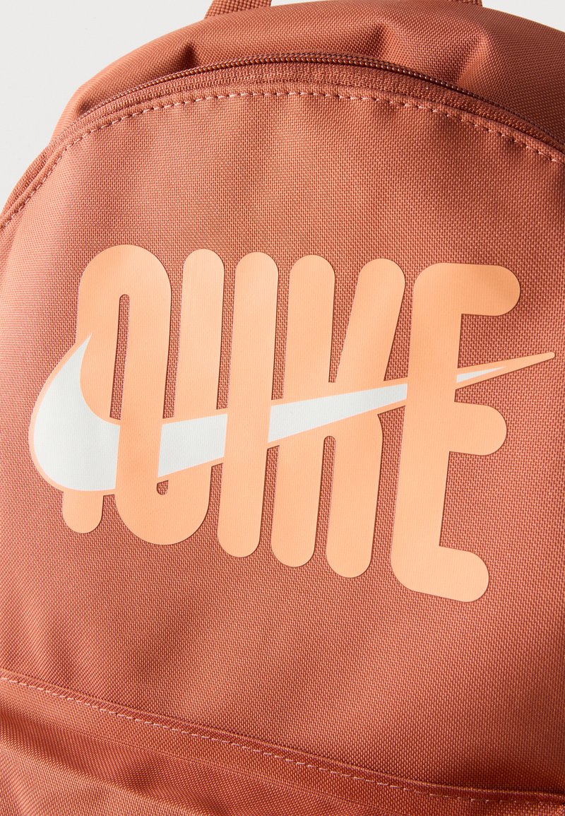 Primer plano de una mochila color óxido con la palabra "NIKE" y un logo blanco con forma de ala impreso en la tela.