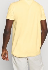 T-shirt giallo a maniche corte con texture morbida, collo rotondo e vestibilità rilassata. Il retro presenta un design semplice con dettagli di orlo ventilato.