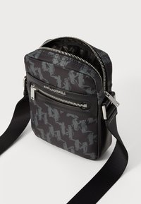 Borsa a tracolla nera in nylon con un motivo astratto testurizzato, dotata di finiture in argento e una tasca frontale con zip per la conservazione.