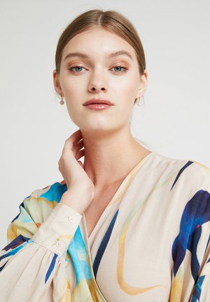 Langärmlige Bluse mit bunten abstrakten Mustern in Blau, Gelb und Orange auf einem hellbeigen Hintergrund; weicher Stoff, V-Ausschnitt, knöpfbare Manschetten.