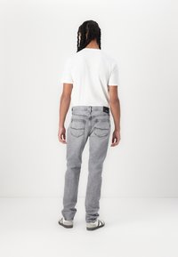 Graue Denim-Jeans mit geradem Schnitt, ausgestattet mit Gesäßtaschen und einem schwarzen Etikett an der Taille. Kombiniert mit einem schlichten weißen T-Shirt.