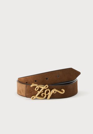Ceinture en daim marron avec une boucle décorative en or en forme des lettres "Z V" dans un design cursif, posée à plat sur une surface blanche.