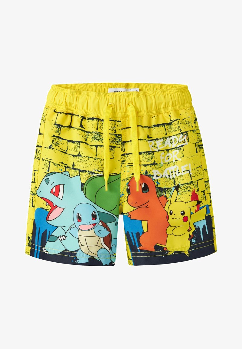 Shorts jaunes avec les personnages Pokémon Bulbizarre, Carapuce, Salamèche et Pikachu, avec le texte "Prêt pour la bataille" sur un fond de mur en briques.