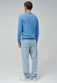 Svetto azzurro chiaro con maniche lunghe e scollatura rotonda, abbinato a jeans chiari a lavaggio leggero e sneakers bianche. Outfit semplice e informale.