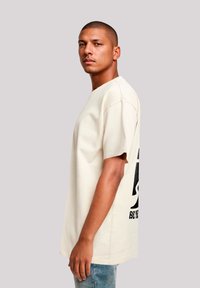 Beige cotton T-shirt with short sleeves, crew neckline, and black graphic print on the back. Styled with light blue denim jeans.