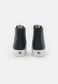 Svarta hög-top sneakers med en slät läderfinish, texturerad tygpanel, vit gummisula och logotyp på baksidan.