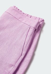 Nahaufnahme von gefalteten, hellvioletten Leinenhosen, die einen elastischen Bund und eine Seitennaht auf einem weißen Hintergrund zeigen.