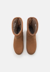 Botas de tobillo de ante marrón con un forro suave y mullido, que cuentan con una cremallera en la parte delantera y un diseño de punta redonda.