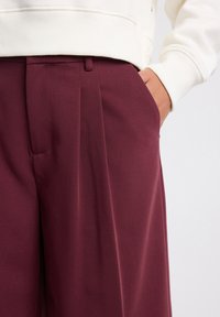 Bordeauxin väriset laskostetut housut, joissa on sileä pinta ja sivutaskut. Yhdistetty valkoiseen collegepaitaan, joka on rentoa mallia.