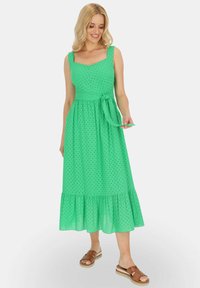 Zielona sukienka do kolan z lekkiego materiału, z kwadratowym dekoltem, szerokimi ramiączkami i falbaną u dołu. Akcent w postaci związanej talii.