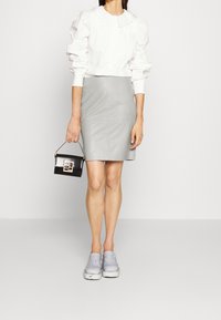 Blusa blanca con mangas fruncidas, falda de cuero gris, zapatos tipo mocasín azul claro y un pequeño bolso negro con herrajes dorados.