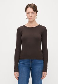 Camisola castanha de mangas longas com decote redondo, design justo e textura suave, acompanhada de uns jeans azuis.