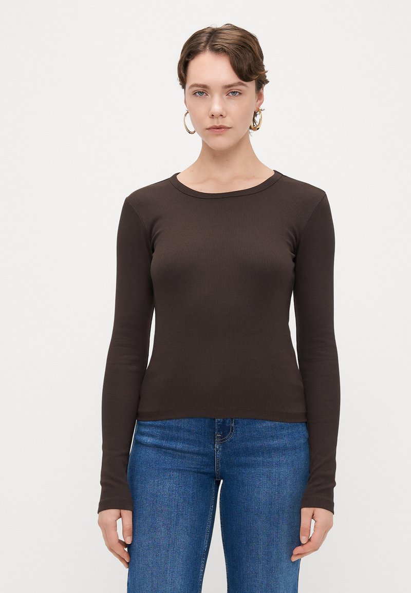 Camisola castanha de mangas longas com decote redondo, design justo e textura suave, acompanhada de uns jeans azuis.