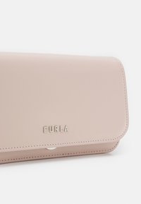 Różowy skórzany portfel o gładkim wykończeniu, z zapięciem na klapę i wytłoczonym logo "FURLA", z detalicznym przeszyciem wzdłuż krawędzi.