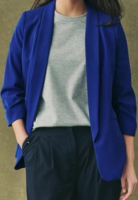 Blauw blazer met een op maat gemaakt ontwerp, gecombineerd met een lichtgrijze T-shirt en donker gestreepte broek. Soepele stoftextuur, casual maar toch professioneel.