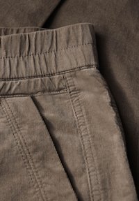 Tissu texturé marron avec une finition douce. Ceinture élastique et couture visible le long des poches et des coutures. Gros plan sur les détails du pantalon.
