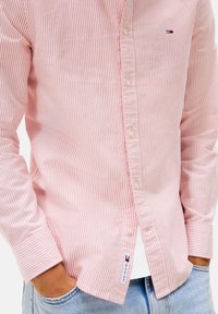 Camisa de botones a rayas rojas y blancas, de material de algodón, con cuello clásico, logo en el pecho y puños abotonados, con un diseño ajustado.