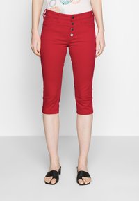 Punaiset lyhyet housut, joissa on istuva malli, viiden napin etusulkemus ja kaksi sivutaskua. Materiaali näyttää joustavalta ja sileältä.