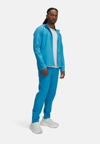 Lyseblå zip-up jakke og matchende bukser lavet af glat, åndbart stof; parret med hvide sneakers; minimalistisk design.