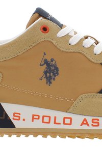 Tan semišové tenisky s bílými tkaničkami, se znakem modrého polo hráče, oranžovými akcenty a bílou a černou podešví.