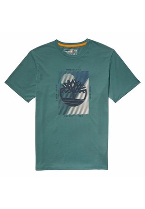 Zielona bawełniana koszulka z krótkim rękawem, z centralnym wzorem przedstawiającym logo drzewa, tekst oraz abstrakcyjne kształty w ciemnoniebieskim i białym kolorze.