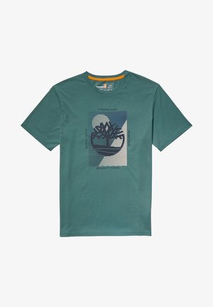 T-shirt en coton vert à manches courtes, avec un graphisme central représentant un logo d'arbre, du texte et des formes abstraites en bleu foncé et blanc cassé.