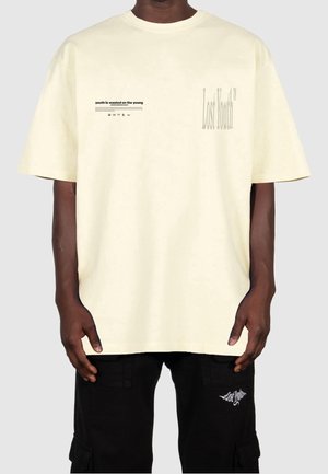 Cremefarbenes Baumwoll-T-Shirt mit dem aufgedruckten Text "Youth is wasted on the young" und dem "Lost Youth"-Logo. Legere Passform, kurze Ärmel.