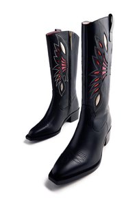 Botas de vaquero de cuero negro con bordados en forma de llamas en rojo, beige y negro, y punteras puntiagudas, mostradas con una bota de frente.