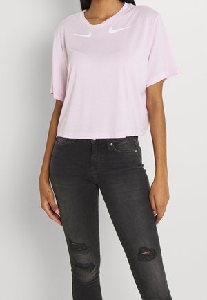 Femme portant un t-shirt Nike rose clair court et un jean skinny noir déchiré, visible des épaules aux chevilles.