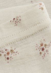 Crème-kleurige stof met een ribbeltextuur, met kleine bloemmotieven in gedempte tinten van roze, oranje en beige.