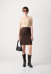 Beige tank top, teksturert brun skjørt, svarte lær cowboy støvler, og liten svart håndveske; solbriller fullfører antrekket.