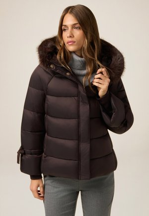 Brun puffjacka med avtagbar huva i päls, horisontell sömnad och justerbara manschetter. I kombination med en grå polotröja.