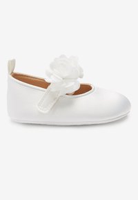 Zapato blanco para bebé con una correa y detalle de flor de tela en la parte superior, suela blanda y tira en la parte trasera sobre un fondo liso.