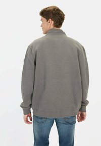 Grå sweatshirt med høj krave, l�øs pasform og ribbede manchetter, parret med blå jeans. Stoffet virker blødt med en ensartet tekstur.