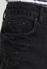 Černé džíny z denimu s opotřebovanými detaily. Mají přední kapsu, měděné nýty a texturovaný pas.