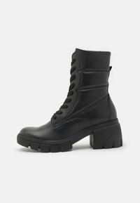 Botín de cuero negro hasta el tobillo con un tacón de bloque grueso, que presenta detalles de cordones, una textura suave y un cuello acolchado para mayor comodidad.