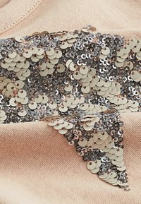 Tela beige con un conjunto denso de parches en forma de estrella hechos de lentejuelas beige y plateadas superpuestas cosidas a ella.
