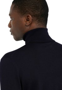 Marineblauwe coltrui van gebreide stof, met een aansluitend ontwerp en geribbelde structuur langs de kraag en schouders.