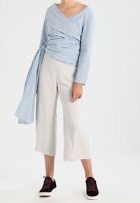 Haut portefeuille à manches longues avec rayures bleues et blanches, associé à un pantalon culotte ample gris clair et des baskets bordeaux.