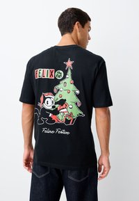 Črno majico s kratkimi rokavi, na kateri je barvit grafični prikaz "Felixa mačka" z božično drevesce in darili, besedilo pa se glasi "Mačje praznično".