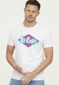 T-shirt en coton blanc avec un logo en diamant bleu et rose portant "Lee Cooper" en police cursive, manches courtes et col rond.