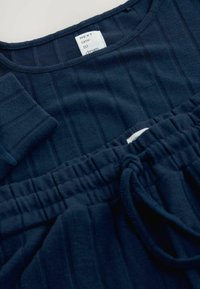 Marineblaues Loungewear-Set mit einem langärmligen Oberteil aus Rippstrick und elastischen Hosen mit einem Kordelzug und vertikalen Streifen.