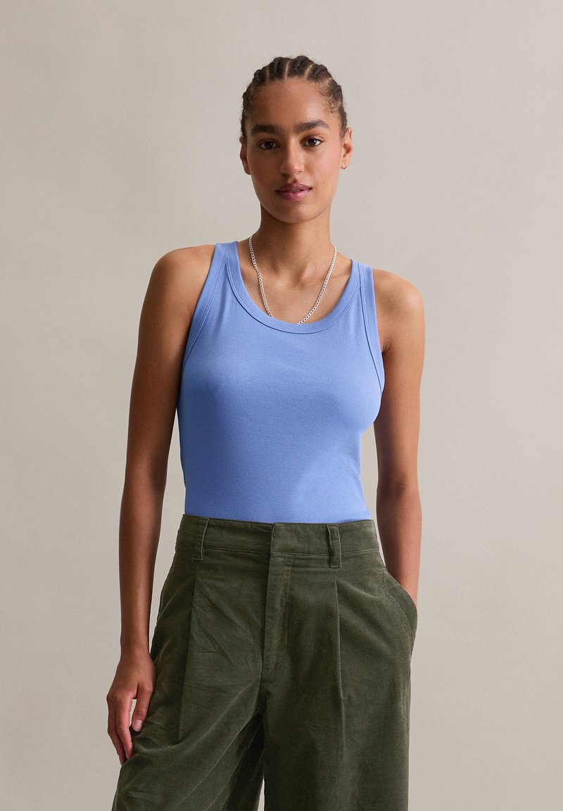 Hellblaues geripptes Tanktop mit rundem Halsausschnitt, kombiniert mit olivgrünen, hoch taillierten Hosen mit Falten und seitlichen Taschen.