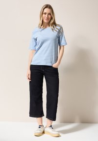 Ljusblå randig t-shirt med korta ärmar, i kombination med mörk denimbyxor med vida ben och vita sneakers med beigefärgad sula.