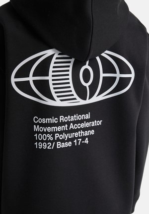 Zwarte hoodie met witte abstracte ovale grafiek en tekst "Cosmic Rotational Movement Accelerator 100% Polyurethane 1992/ Base 17-4" op de achterkant.