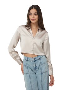 Blusa in seta tagliata in un beige chiaro con colletto e chiusura a bottoni. Le maniche lunghe presentano polsini con bottoni.