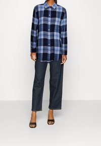 Blue and black plaid shirt with long sleeves and button front, paired with dark denim wide-leg pants and black open-toe heels.